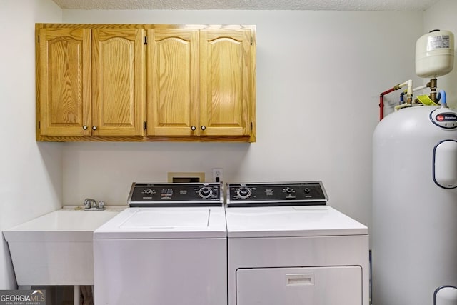 clothes washing area featuring water heater, sink, cabinets, and washer and dryer