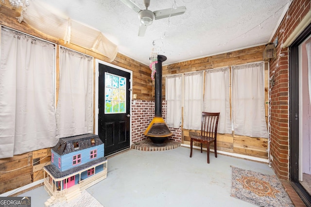 interior space featuring ceiling fan, a wood stove, a textured ceiling, and concrete floors