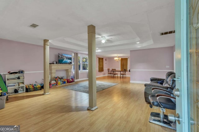 workout room featuring hardwood / wood-style floors, ceiling fan with notable chandelier, and a raised ceiling