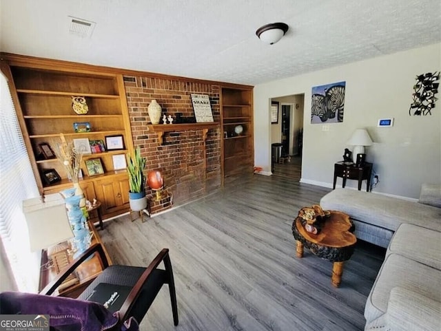 living room with built in shelves, a brick fireplace, a textured ceiling, and hardwood / wood-style flooring