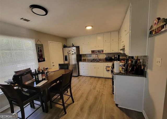 kitchen with stainless steel refrigerator with ice dispenser, light hardwood / wood-style flooring, sink, white cabinets, and decorative backsplash