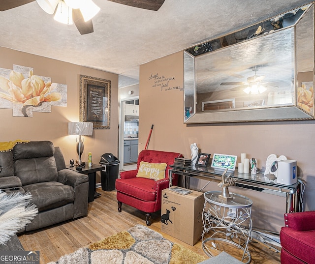 living room with ceiling fan, light hardwood / wood-style flooring, and a textured ceiling