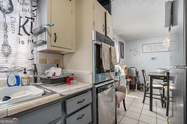 kitchen featuring light tile patterned floors, a textured ceiling, gray cabinets, and stainless steel appliances