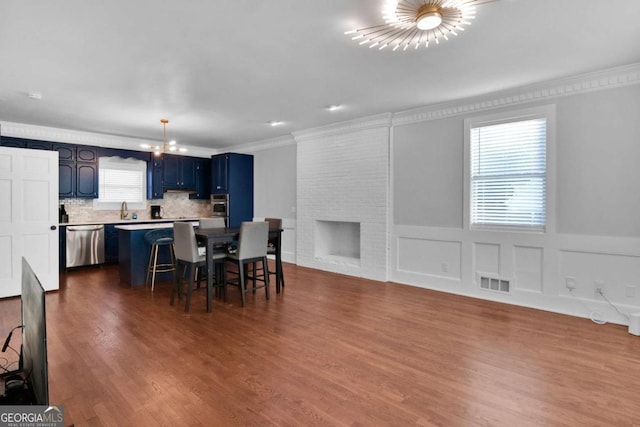 dining space with sink, a brick fireplace, an inviting chandelier, wood-type flooring, and ornamental molding