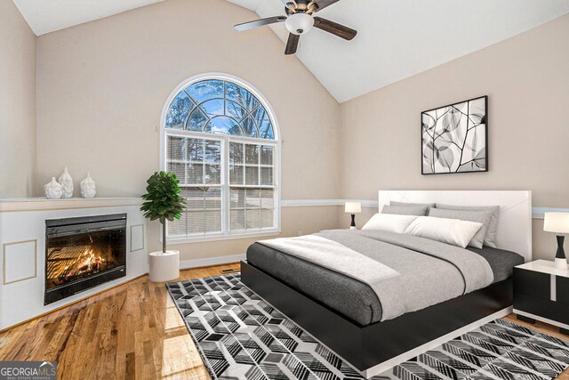 bedroom featuring lofted ceiling, ceiling fan, wood finished floors, baseboards, and a glass covered fireplace