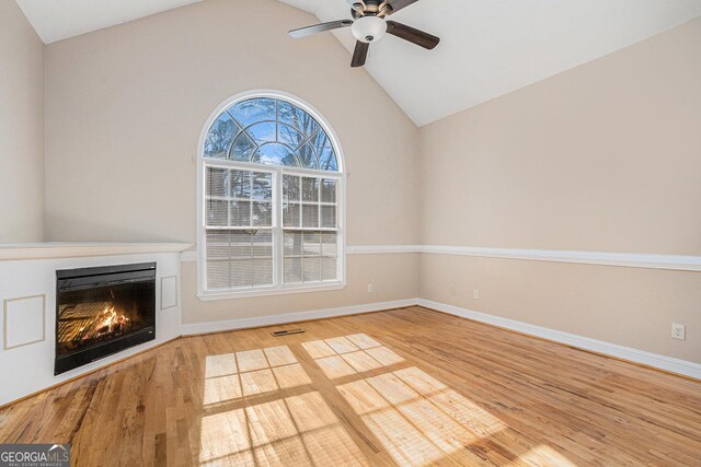 unfurnished living room with lofted ceiling, a warm lit fireplace, baseboards, and wood finished floors