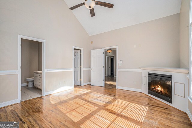 unfurnished living room with baseboards, high vaulted ceiling, wood finished floors, and a glass covered fireplace