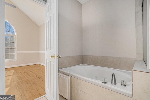 bathroom featuring lofted ceiling, baseboards, a whirlpool tub, and wood finished floors