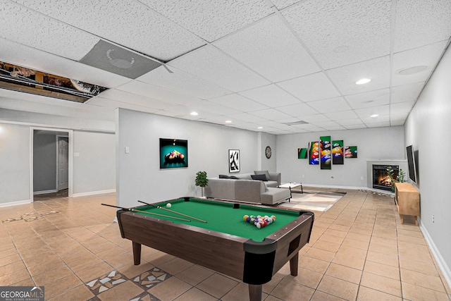 recreation room with recessed lighting, tile patterned flooring, a warm lit fireplace, a drop ceiling, and baseboards