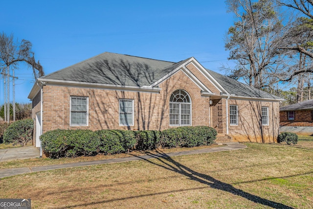 view of front facade with brick siding, a front yard, and a shingled roof