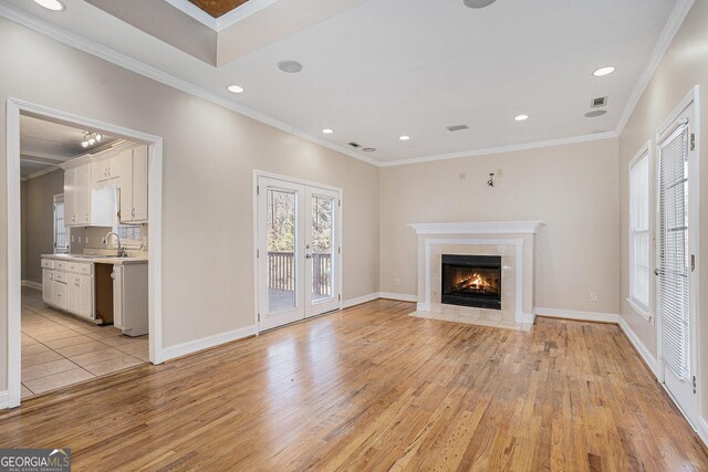 unfurnished living room featuring a tile fireplace, french doors, sink, light wood-type flooring, and ornamental molding