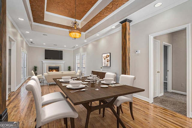 dining area with a tray ceiling, a fireplace, light wood-type flooring, and ornamental molding