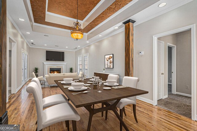 dining space with light wood-style floors, a raised ceiling, a lit fireplace, and ornate columns