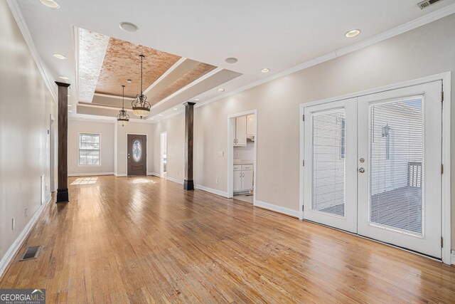 entrance foyer with light hardwood / wood-style floors, ornamental molding, french doors, and a tray ceiling