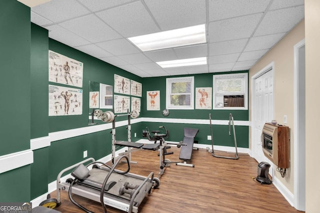 exercise room with wood-type flooring, heating unit, and a drop ceiling