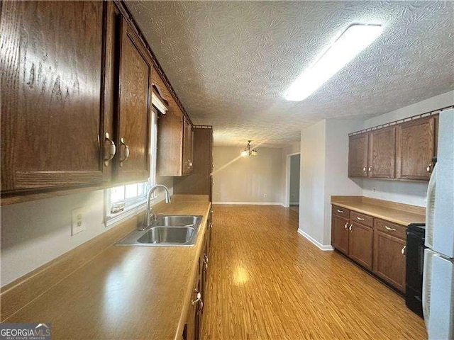 kitchen with black range oven, a textured ceiling, sink, white fridge, and light hardwood / wood-style floors