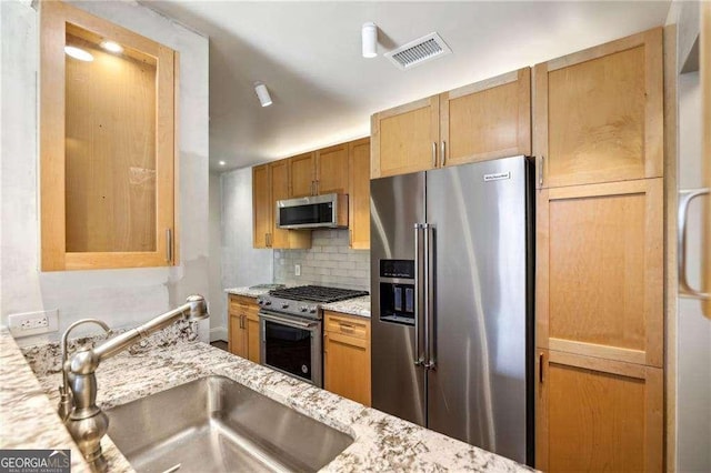 kitchen featuring backsplash, light stone counters, sink, and stainless steel appliances