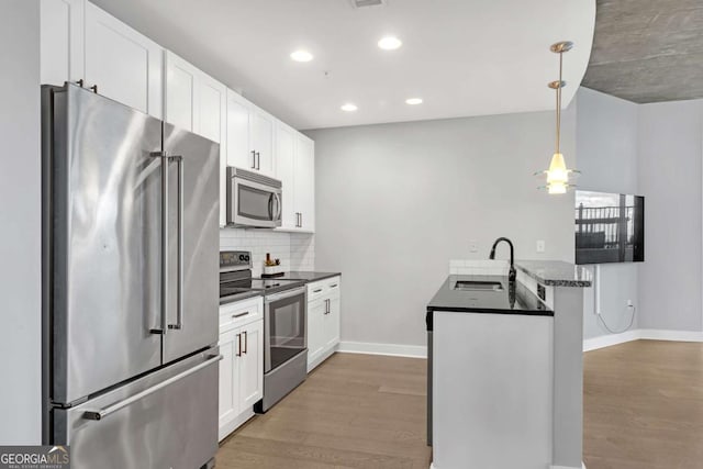 kitchen with kitchen peninsula, appliances with stainless steel finishes, sink, white cabinets, and hanging light fixtures