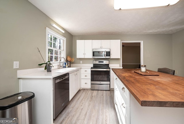 kitchen featuring white cabinetry, sink, stainless steel appliances, wooden counters, and light wood-type flooring