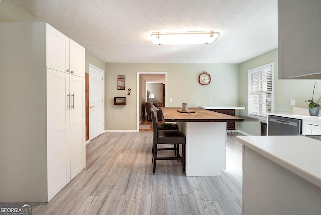 kitchen featuring wooden counters, a breakfast bar, light hardwood / wood-style flooring, dishwasher, and white cabinets