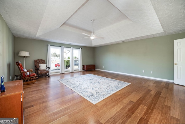 interior space with a raised ceiling, ceiling fan, a textured ceiling, and hardwood / wood-style flooring