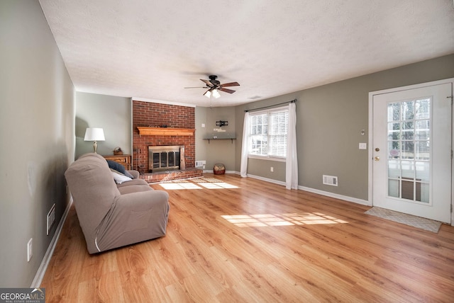 living room featuring a textured ceiling, light wood-type flooring, a brick fireplace, and ceiling fan