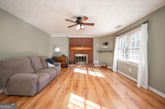 living room featuring light wood-type flooring, a textured ceiling, a brick fireplace, and ceiling fan