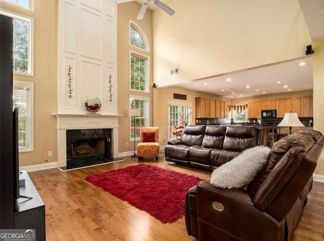 living room with a fireplace, a high ceiling, ceiling fan, and wood-type flooring