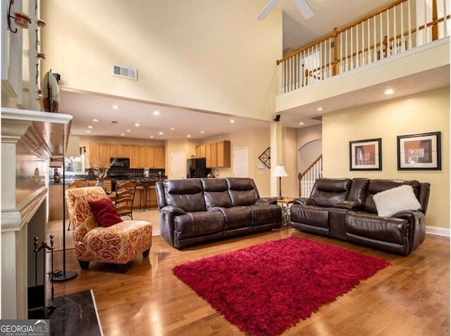 living room featuring hardwood / wood-style flooring, ceiling fan, and a towering ceiling