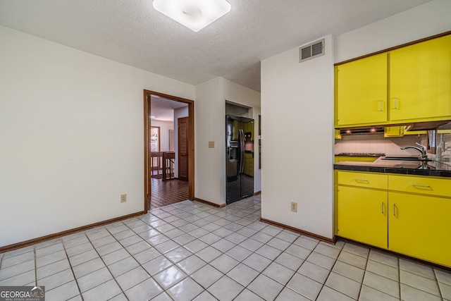 kitchen featuring a textured ceiling, sink, light tile patterned flooring, backsplash, and black fridge with ice dispenser