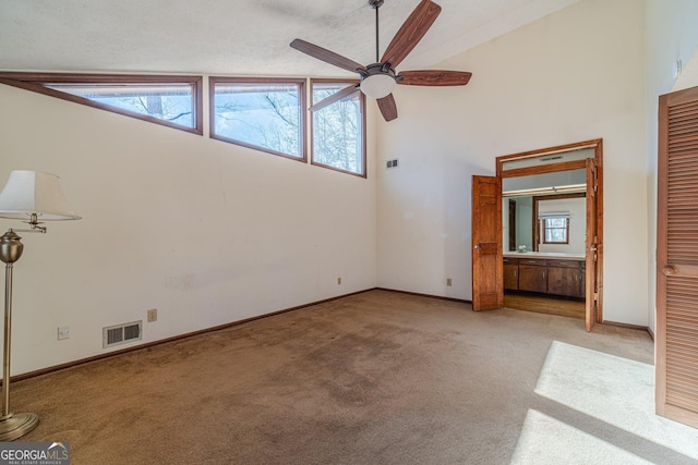 unfurnished living room with ceiling fan, high vaulted ceiling, a textured ceiling, and light carpet