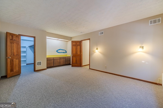 unfurnished bedroom featuring light colored carpet, a textured ceiling, a closet, and a walk in closet