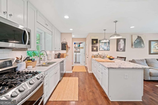 kitchen with appliances with stainless steel finishes, dark wood-type flooring, sink, white cabinets, and hanging light fixtures