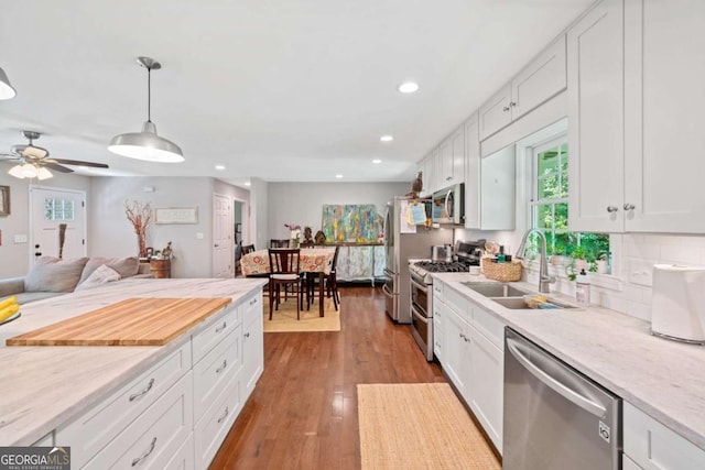 kitchen with decorative light fixtures, stainless steel appliances, white cabinetry, and sink