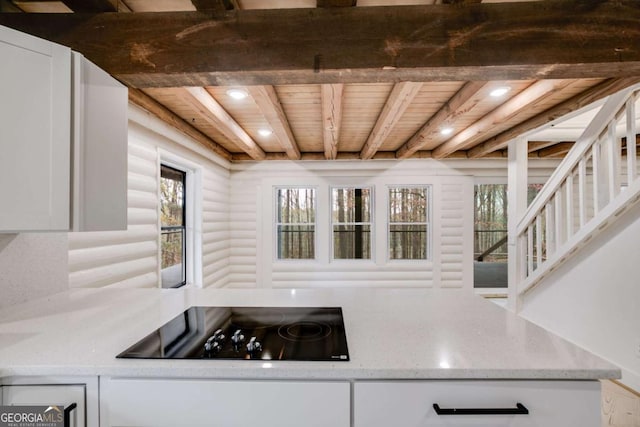 kitchen featuring black electric stovetop, rustic walls, beamed ceiling, white cabinetry, and wood ceiling