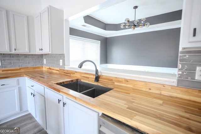 kitchen with butcher block counters, sink, hanging light fixtures, a chandelier, and white cabinets