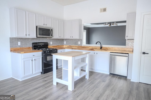 kitchen with stainless steel appliances, white cabinetry, butcher block counters, and sink