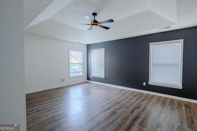 spare room featuring a tray ceiling, ceiling fan, and dark wood-type flooring