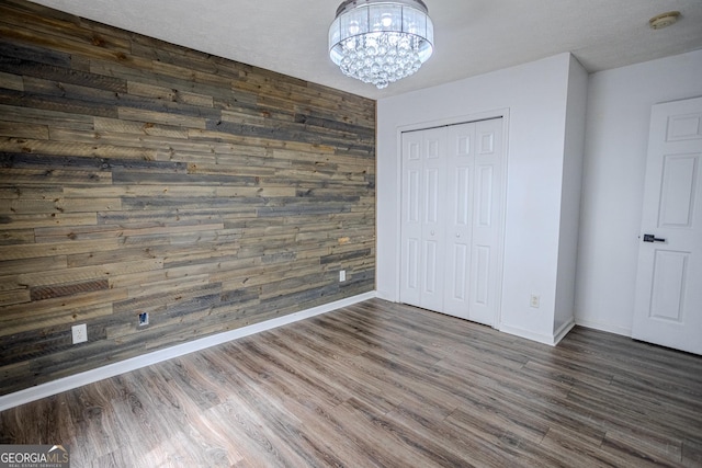 unfurnished bedroom with an inviting chandelier, a closet, dark wood-type flooring, and wood walls