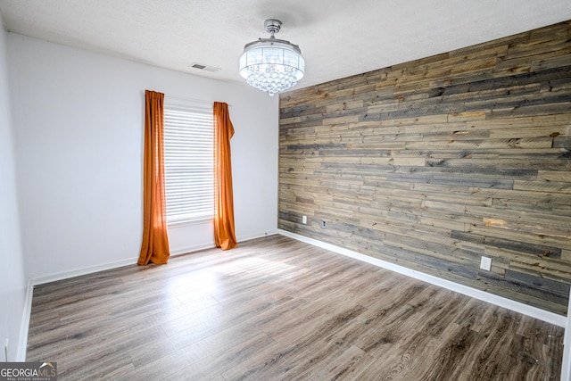 unfurnished room with hardwood / wood-style floors, a notable chandelier, a textured ceiling, and wooden walls