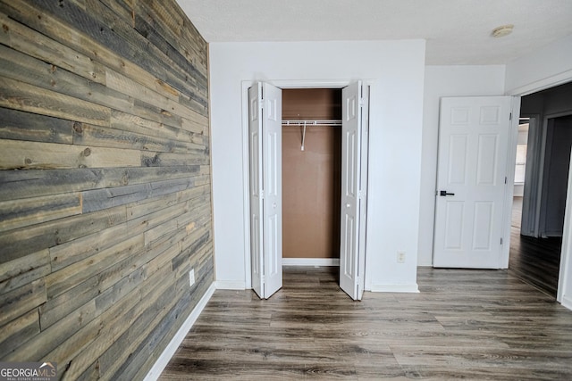 unfurnished bedroom with wood walls, a closet, and dark hardwood / wood-style floors