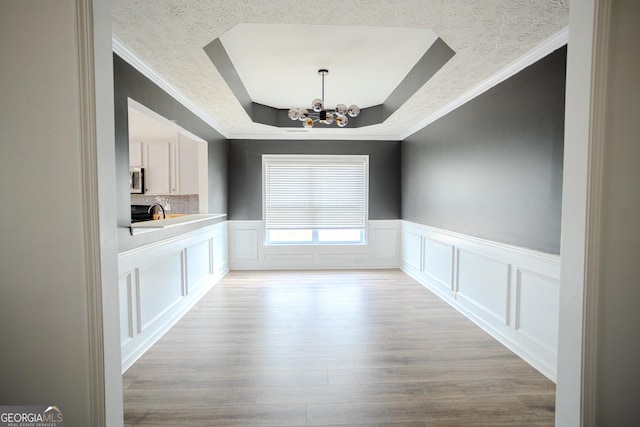 unfurnished dining area featuring crown molding, light hardwood / wood-style flooring, a textured ceiling, a tray ceiling, and a notable chandelier