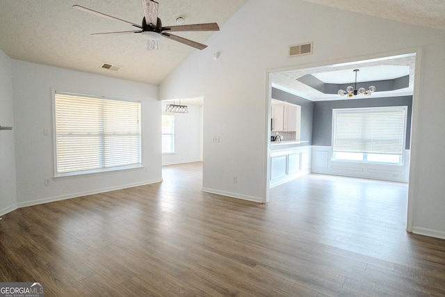 unfurnished living room featuring vaulted ceiling, a textured ceiling, wood-type flooring, and ceiling fan with notable chandelier