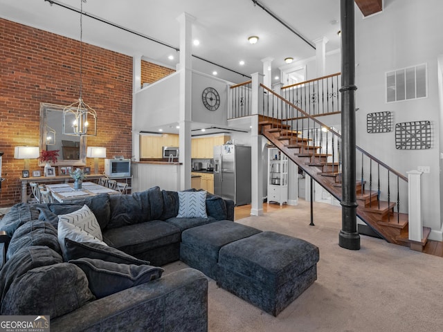 living room featuring a notable chandelier, a towering ceiling, light carpet, and brick wall