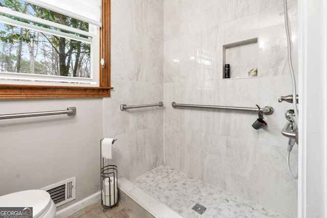 bathroom featuring toilet, tile patterned flooring, and tiled shower