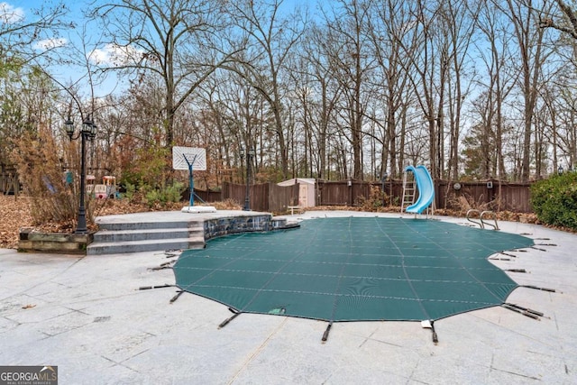 view of swimming pool with a storage unit, a patio area, and a water slide