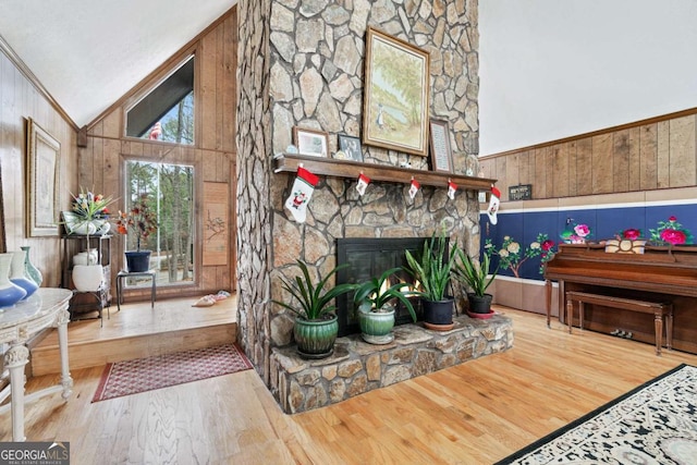 interior space with hardwood / wood-style flooring, wooden walls, a stone fireplace, and high vaulted ceiling