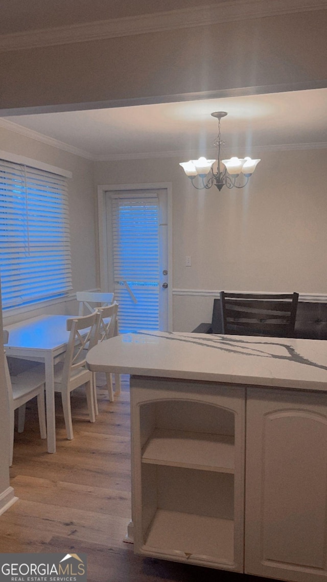 kitchen featuring a notable chandelier, light wood-type flooring, pendant lighting, crown molding, and white cabinets