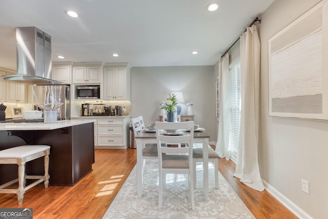 kitchen featuring a breakfast bar, stainless steel appliances, white cabinetry, and wall chimney exhaust hood