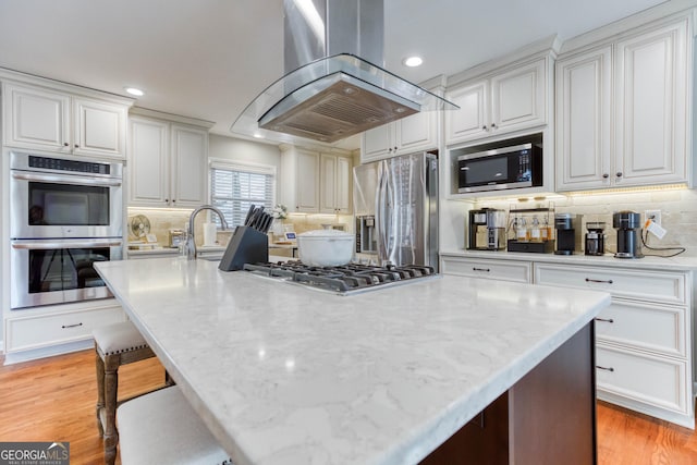 kitchen with island exhaust hood, appliances with stainless steel finishes, and white cabinetry